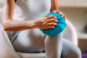 Knee pain treatment. Woman holding an ice bag pack on her painful knee